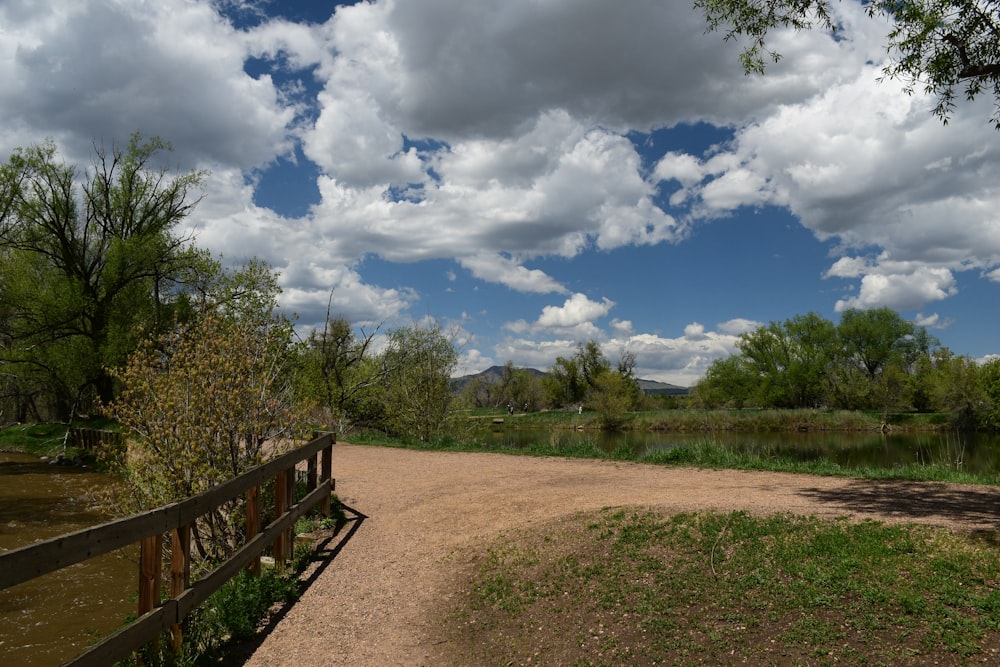 a dirt road next to a river under a cloudy sky