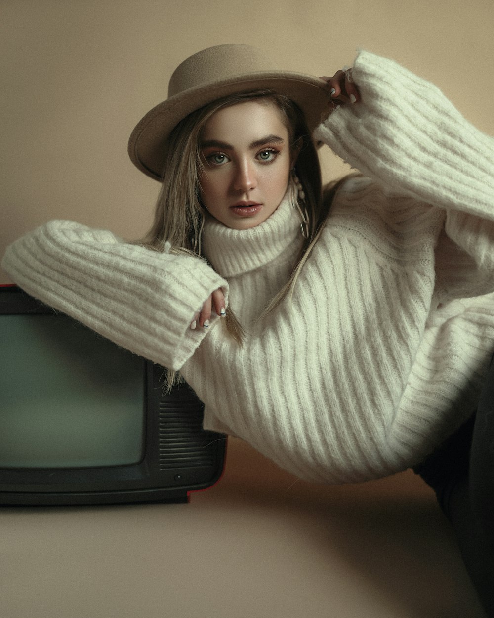 Uma mulher de suéter branco e chapéu encostado em uma TV