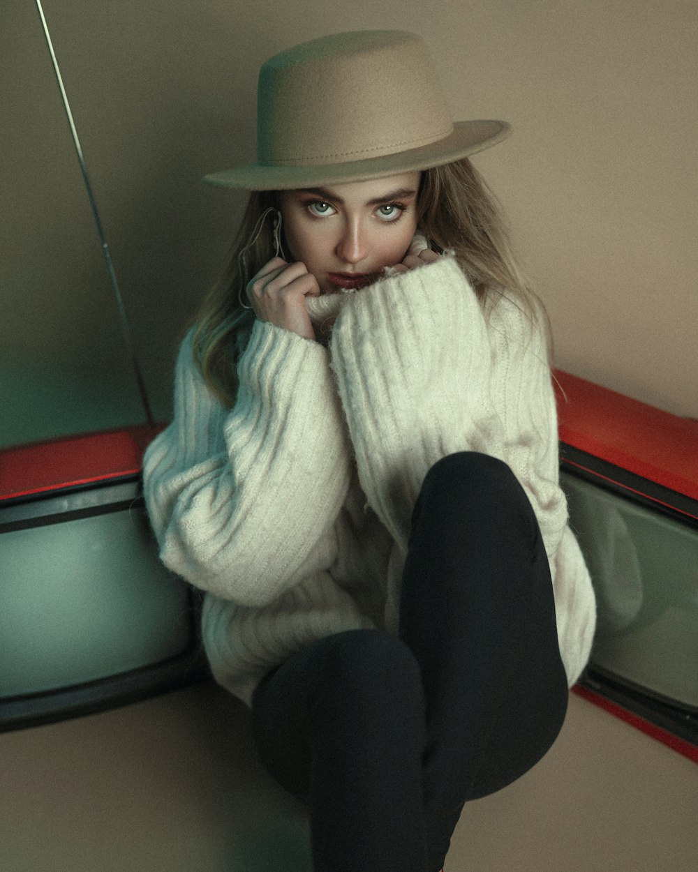 a woman in a white sweater and hat sitting on a red car