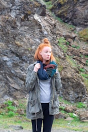 a woman with red hair is standing in front of a mountain