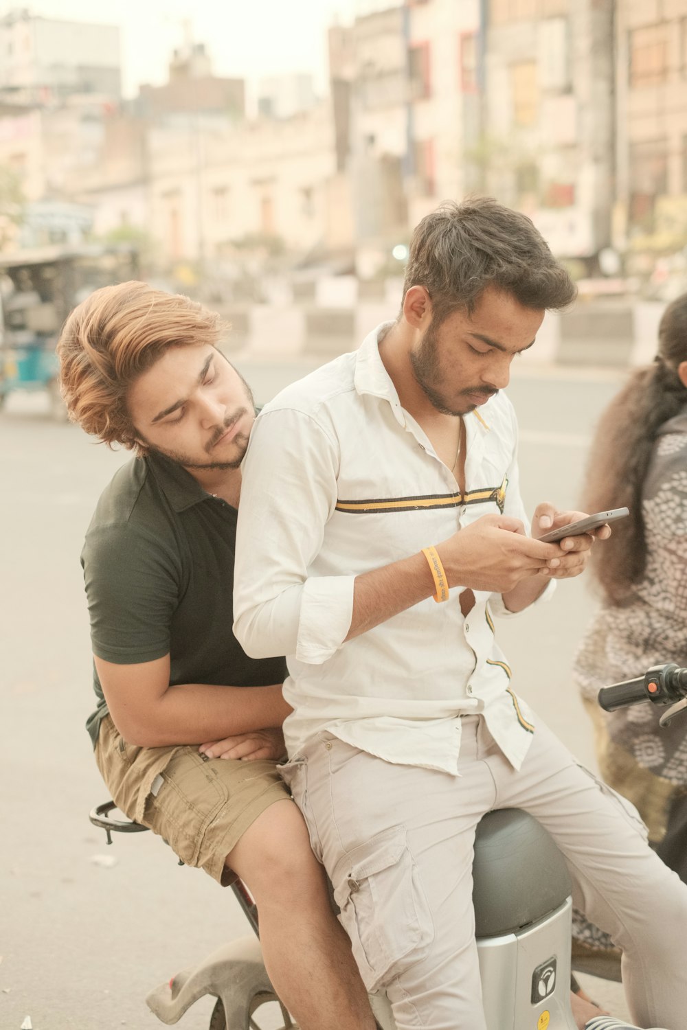 two men sitting on a motorcycle looking at a cell phone