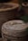 A close-up view of a terracotta pot with a rustic finish. On top of the pot, a small white flower and a dried leaf are carefully placed. The background features more earthen pots, slightly out of focus.