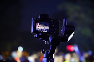 A camera mounted on a stabilizer is capturing a scene. The screen on the camera displays a colorful crowd with bright lighting, suggesting an event or performance is taking place.