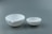 Two white ceramic bowls with pouring spouts sit side by side against a muted gray background. The bowls differ in size, with the larger one on the left and the smaller one on the right.