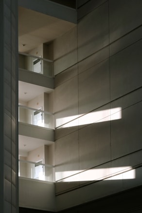 A multi-level interior space with an emphasis on geometric design. Sunlight streams through, casting angular shadows across the concrete surfaces. The minimalist architecture features clean lines and open balconies.