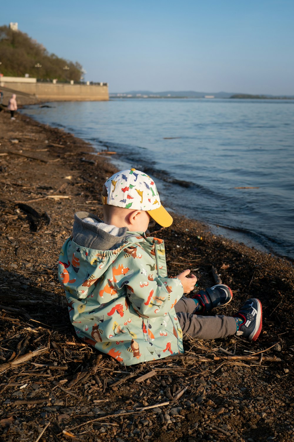 a small child sitting on a beach next to a body of water