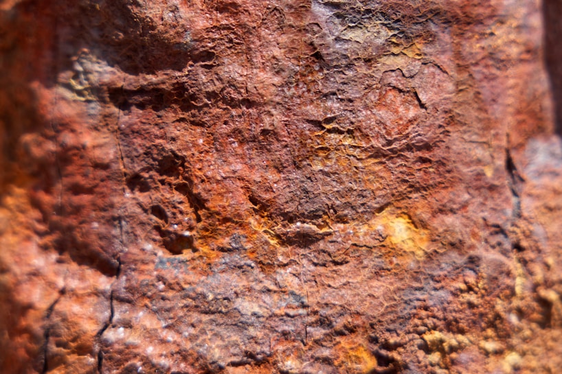A close-up view of a textured surface with various shades of reddish-brown and orange. The surface appears rough and irregular, with visible cracks and crevices, suggesting it might be rust or a similar corrosive material.