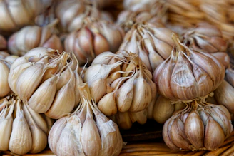 Fresh garlic bulbs with papery skins resting on a woven basket, surrounded by green leaves.