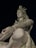 A large statue of a deity in a meditative pose with closed eyes, intricate details including ornaments and a serene expression on the face. The statue is illuminated against a dark background, highlighting the smooth texture and craftsmanship.