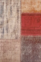 Close-up view of a textured fabric or carpet with a patchwork design consisting of four squares. The squares have different patterns and colors including beige, red, and brown. The red square has visible stitching along its borders.