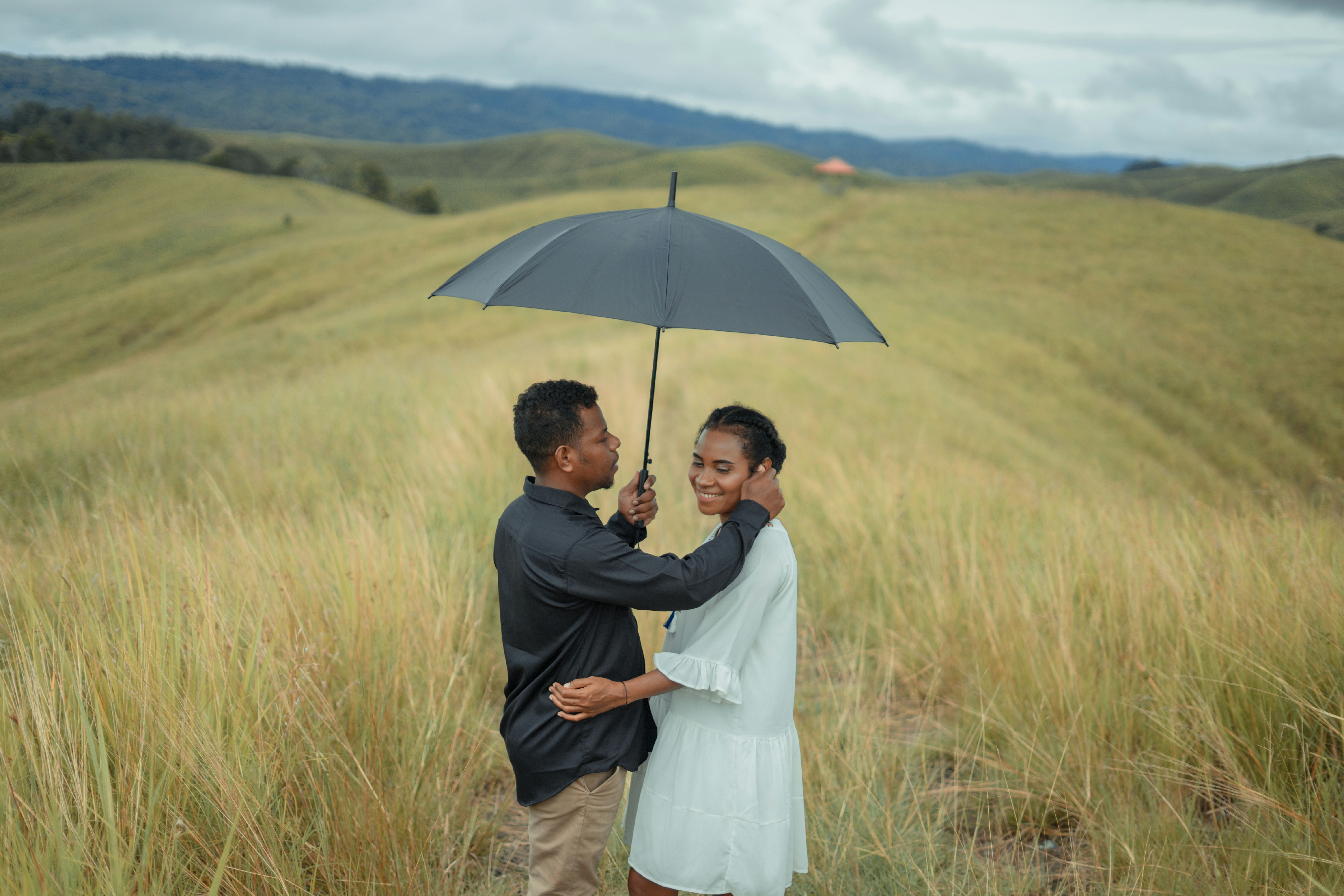 a man and woman standing under an umbrella in a field