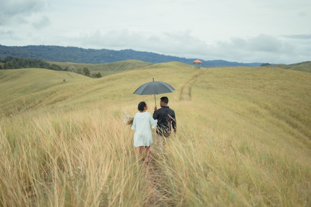 a man and a woman walking in a field with an umbrella