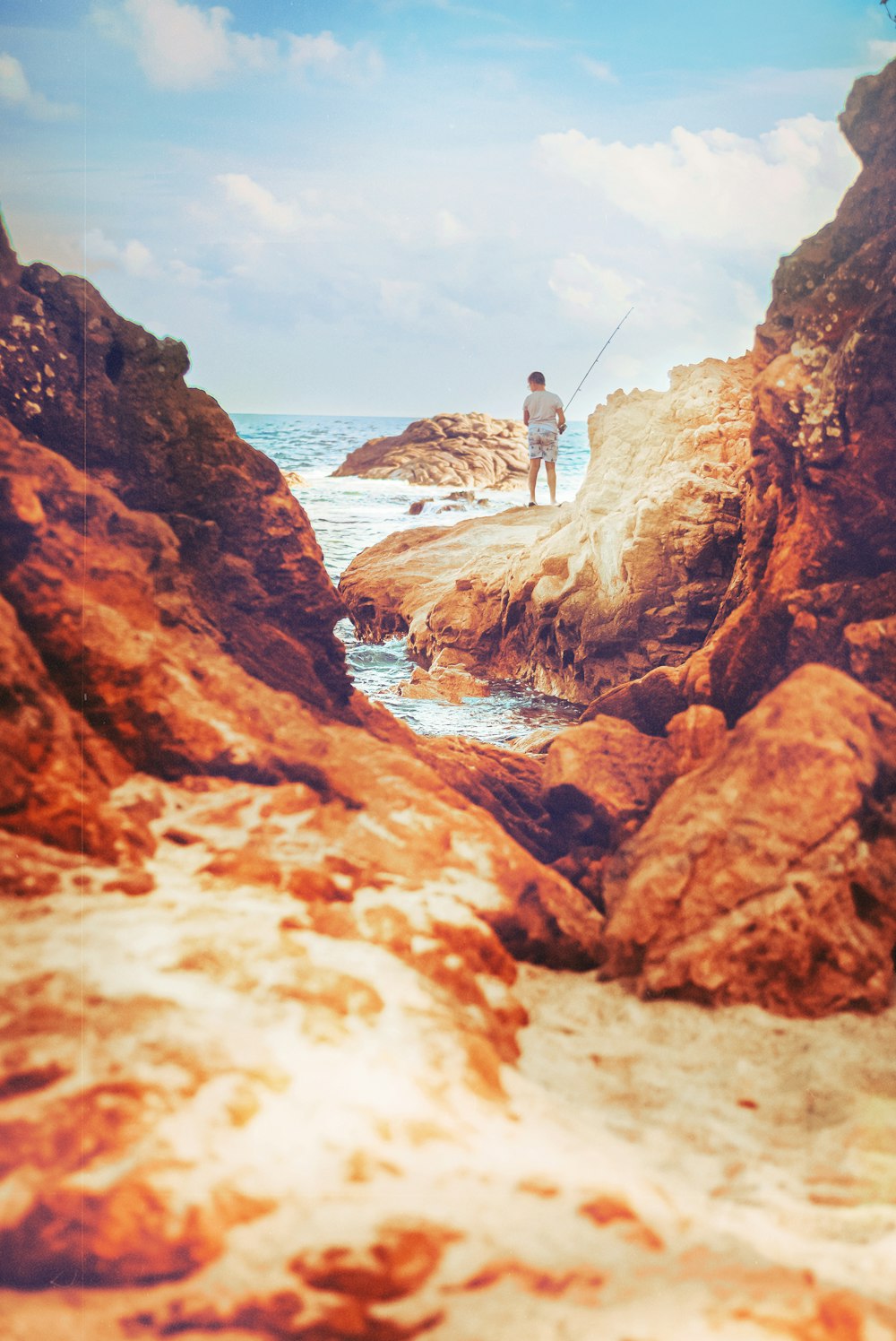 a man standing on top of a rocky beach next to the ocean