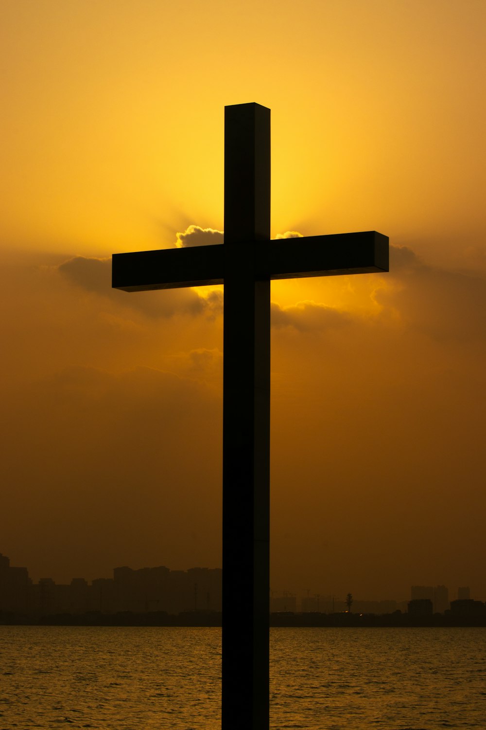 a cross is silhouetted against a sunset over a body of water