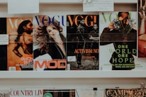 A collection of magazines is displayed on a shelf. The magazines feature various covers with different themes. One cover highlights an athlete, another depicts a smiling woman, and others focus on activism and nature themes. The branding and imagery suggest the publications are fashion and lifestyle-oriented.