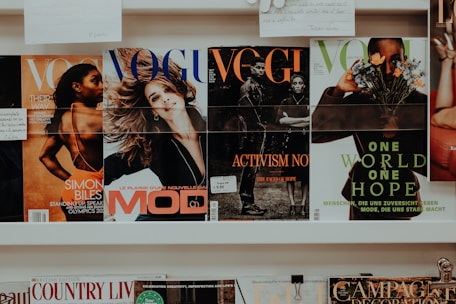 A collection of magazines is displayed on a shelf. The magazines feature various covers with different themes. One cover highlights an athlete, another depicts a smiling woman, and others focus on activism and nature themes. The branding and imagery suggest the publications are fashion and lifestyle-oriented.