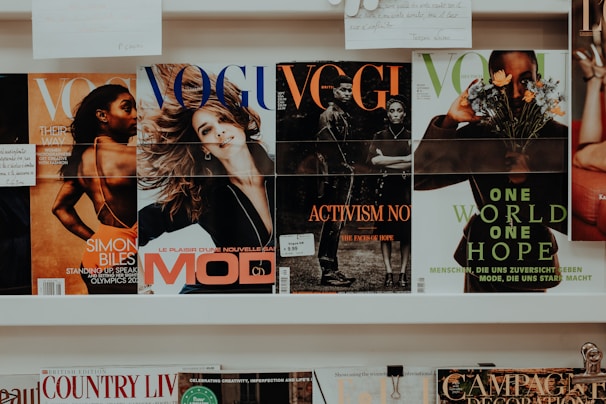 A collection of magazines is displayed on a shelf. The magazines feature various covers with different themes. One cover highlights an athlete, another depicts a smiling woman, and others focus on activism and nature themes. The branding and imagery suggest the publications are fashion and lifestyle-oriented.