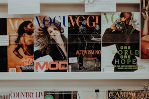 A collection of magazines is displayed on a shelf. The magazines feature various covers with different themes. One cover highlights an athlete, another depicts a smiling woman, and others focus on activism and nature themes. The branding and imagery suggest the publications are fashion and lifestyle-oriented.