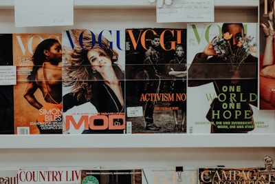 A collection of magazines is displayed on a shelf. The magazines feature various covers with different themes. One cover highlights an athlete, another depicts a smiling woman, and others focus on activism and nature themes. The branding and imagery suggest the publications are fashion and lifestyle-oriented.