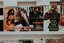 A collection of magazines is displayed on a shelf. The magazines feature various covers with different themes. One cover highlights an athlete, another depicts a smiling woman, and others focus on activism and nature themes. The branding and imagery suggest the publications are fashion and lifestyle-oriented.
