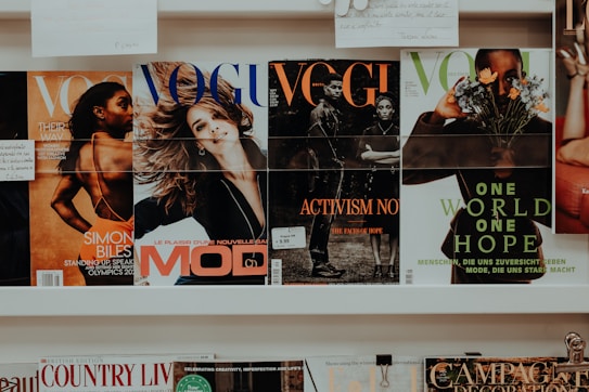 A collection of magazines is displayed on a shelf. The magazines feature various covers with different themes. One cover highlights an athlete, another depicts a smiling woman, and others focus on activism and nature themes. The branding and imagery suggest the publications are fashion and lifestyle-oriented.