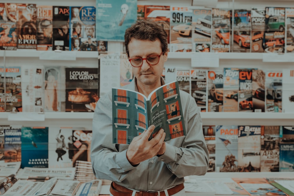 a man reading a book in front of a wall of magazines