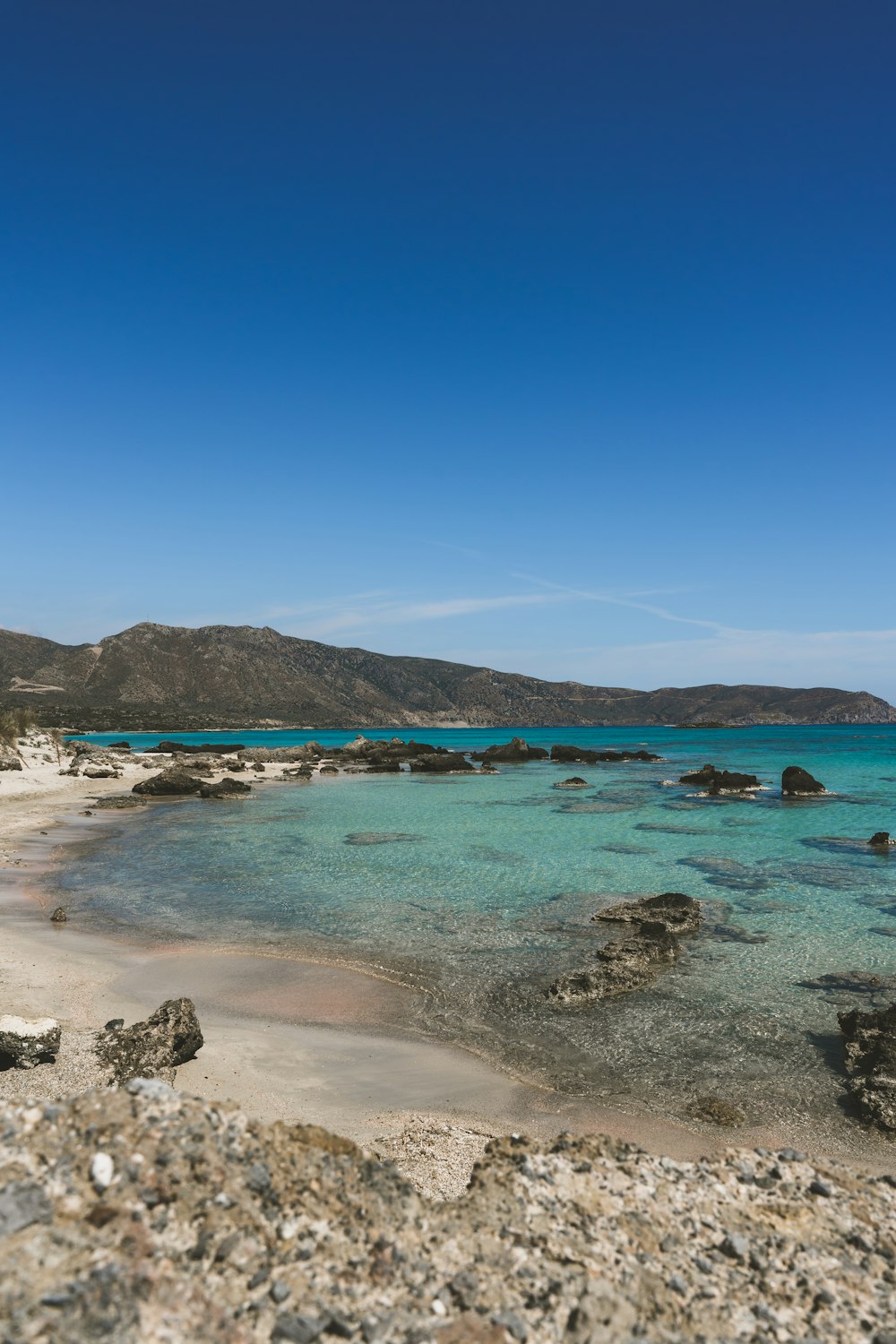 a sandy beach with clear blue water and mountains in the background