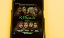 A smartphone screen displays a movie poster featuring a group of women, some wearing hijabs, with serious and contemplative expressions alongside smiling faces.