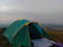A camper setting up a sturdy tent at dusk with rain clouds gathering.