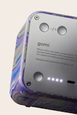 A close-up view of a device featuring a smooth metallic surface with buttons and text. The casing has a colorful marbled pattern. The text includes branding and a message about using recycled materials.