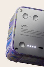 A close-up view of a device featuring a smooth metallic surface with buttons and text. The casing has a colorful marbled pattern. The text includes branding and a message about using recycled materials.