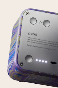 A close-up view of a device featuring a smooth metallic surface with buttons and text. The casing has a colorful marbled pattern. The text includes branding and a message about using recycled materials.