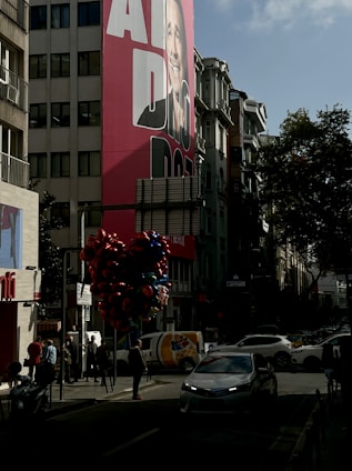 A happy gig worker standing next to their car wrapped with a colorful advertisement in a busy city street.