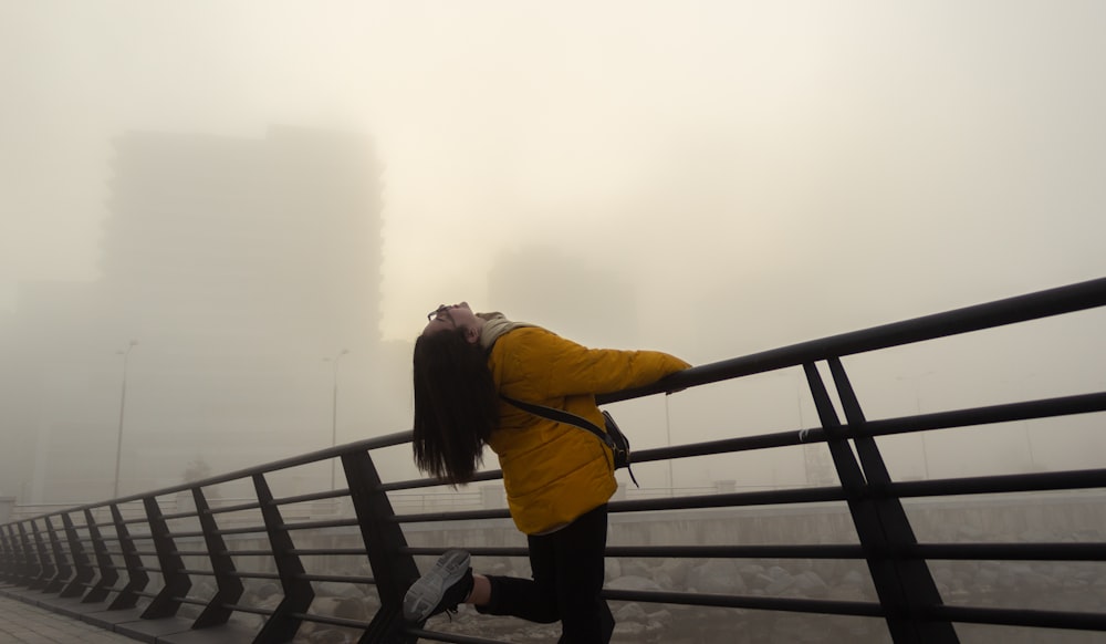 a woman in a yellow jacket leaning on a rail