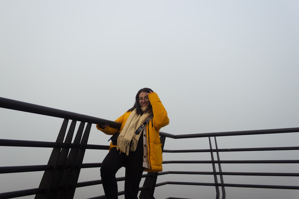 eine Frau in einer gelben Jacke, die auf einem Geländer steht