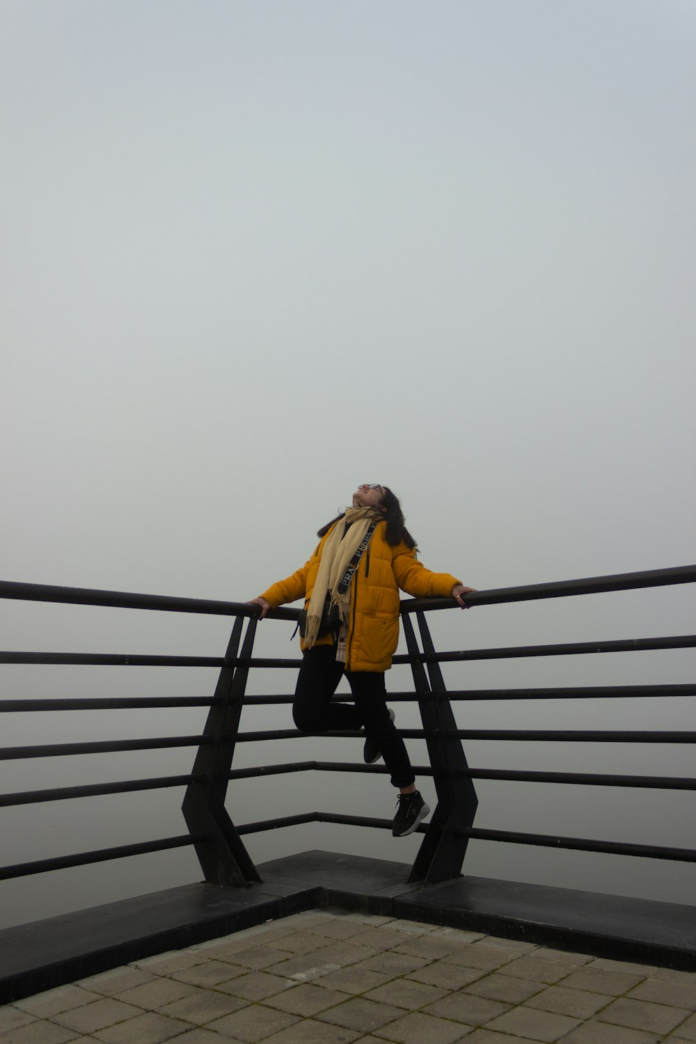 a woman in a yellow jacket is standing on a railing