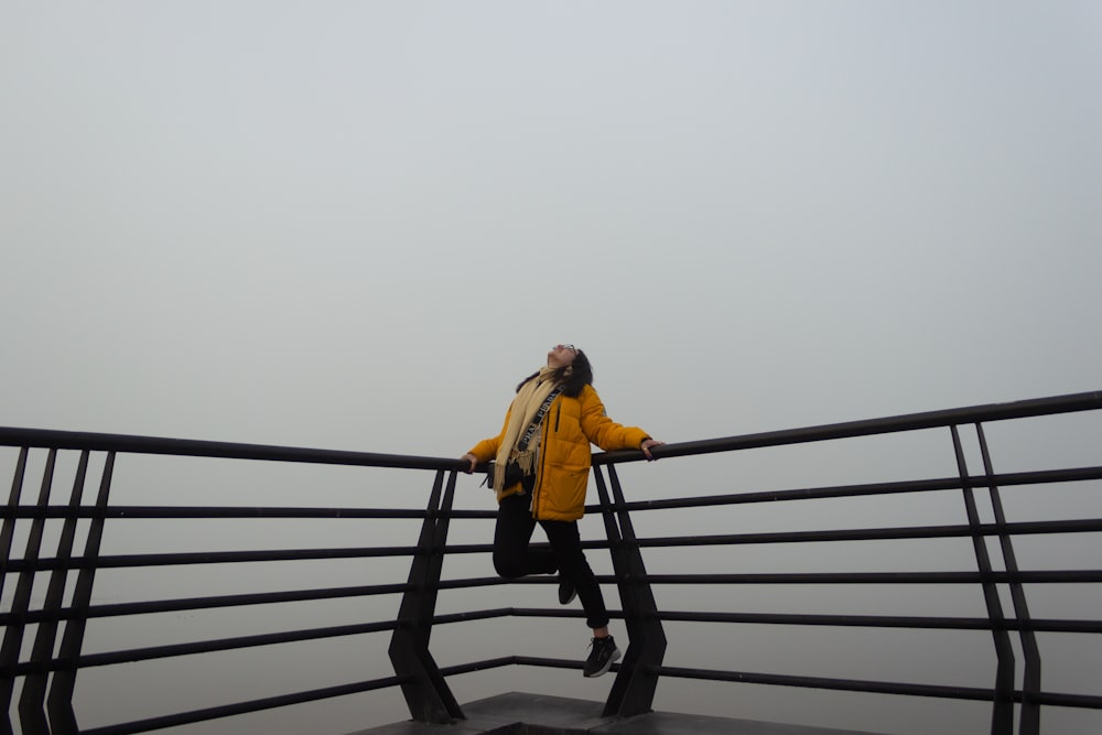 Une femme en veste jaune se tient debout sur une balustrade