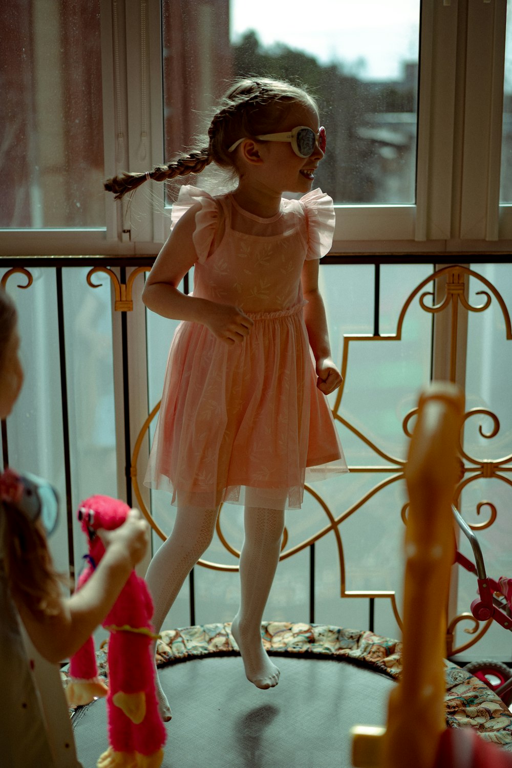 a little girl in a pink dress standing next to a window