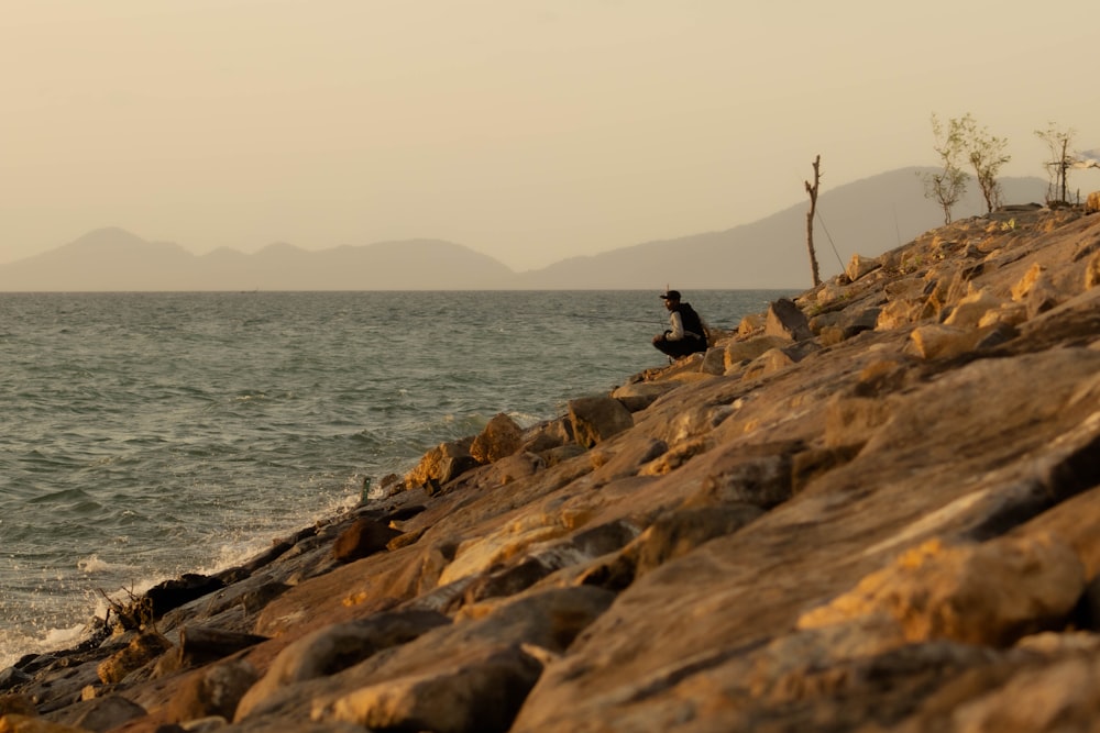 a man sitting on a rock next to the ocean