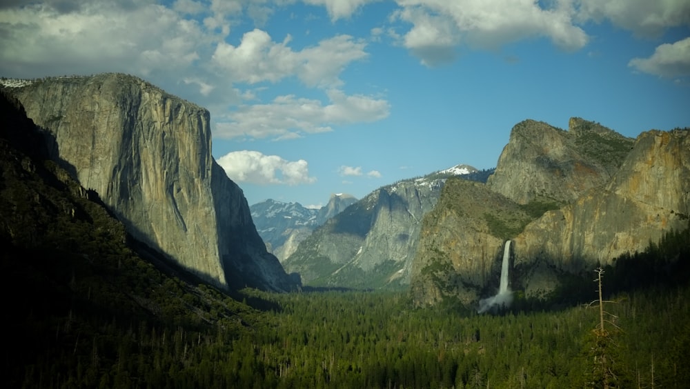 a view of a valley with a waterfall and mountains in the background