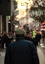 Man wearing a deep green velvet cap walking through a sunlit city street in autumn