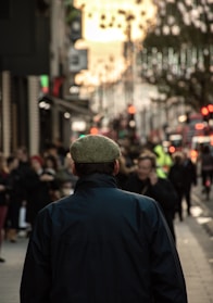 Man wearing a deep green velvet cap walking through a sunlit city street in autumn