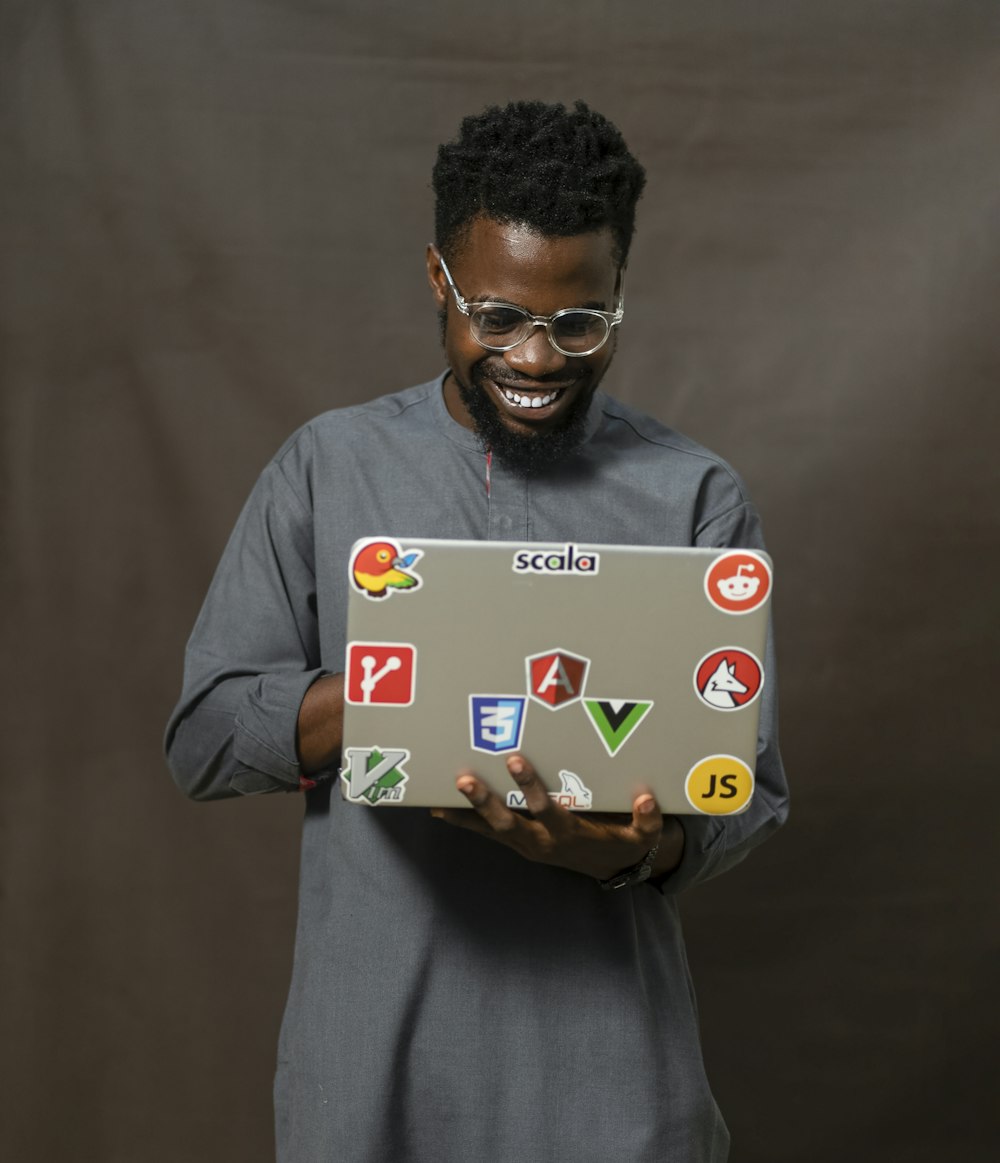 a man holding a laptop with a lot of stickers on it