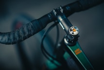A close-up view of a bicycle handlebar featuring intricate patterned grips and a detailed stem cap with colorful accents. The handlebars display a textured geometric design, and the stem cap includes branding and a vibrant orange detail.