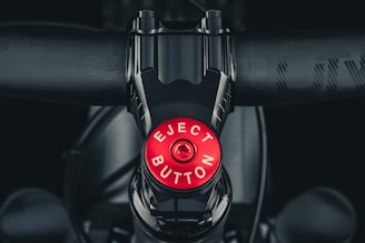 A central view of a bicycle stem with a prominently displayed red 'Eject Button' for comedic effect. The bicycle's handlebars and other parts are visible in a metallic and matte black finish.