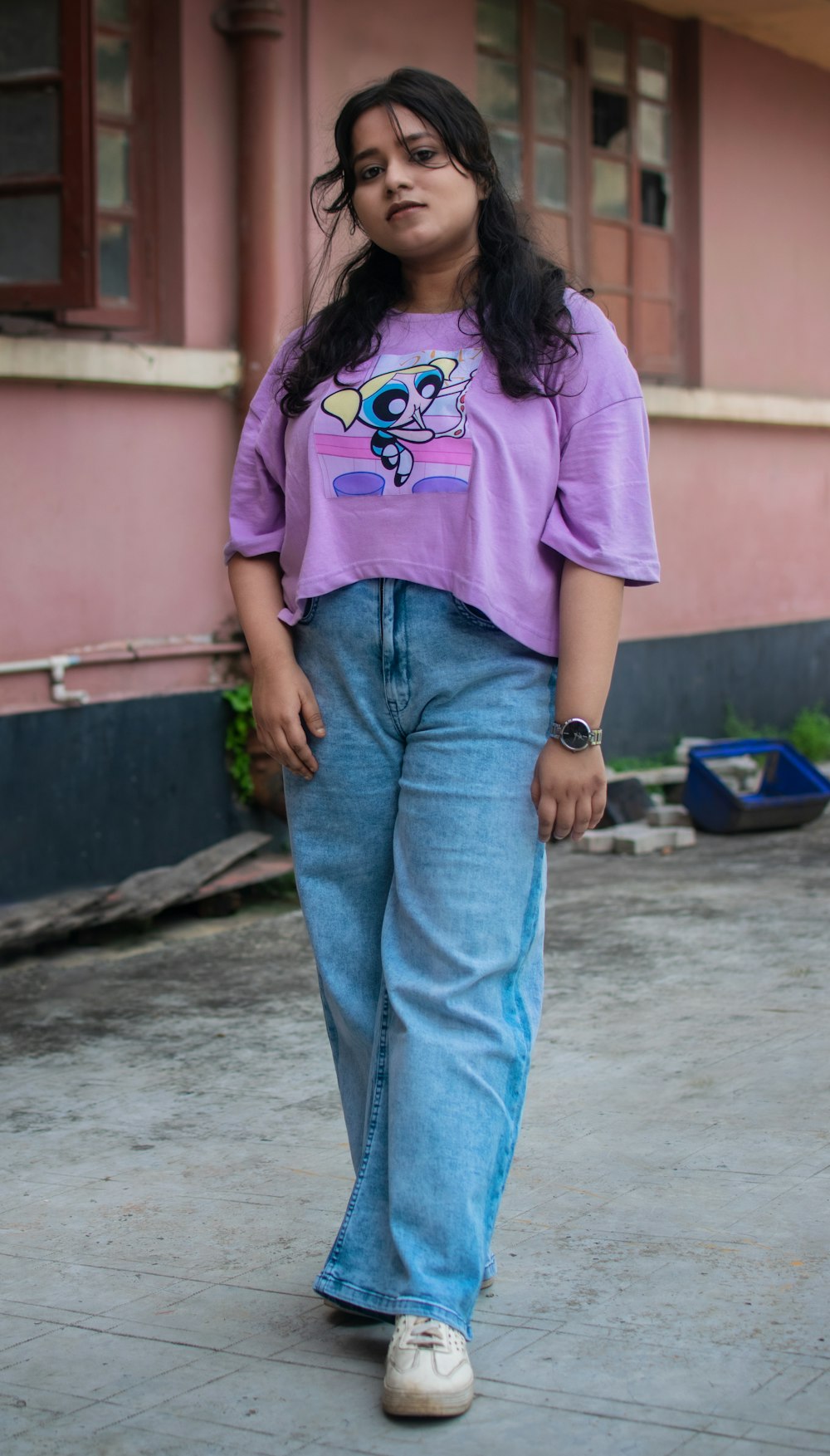 a woman wearing a purple shirt and jeans standing in front of a pink building