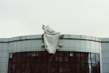 A building with a curved facade features a large, partially covered sign. A white sheet is draped over the top of the building, obscuring some of the text. The architecture is contemporary with reflective windows.