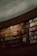 A large curved bookshelf filled with an array of colorful books. The shelves are stacked with volumes of varying sizes and colors, creating a visually rich tapestry. The setting is dimly lit, suggesting a quiet, introspective atmosphere. The architecture of the shelves suggests a library or study room environment.