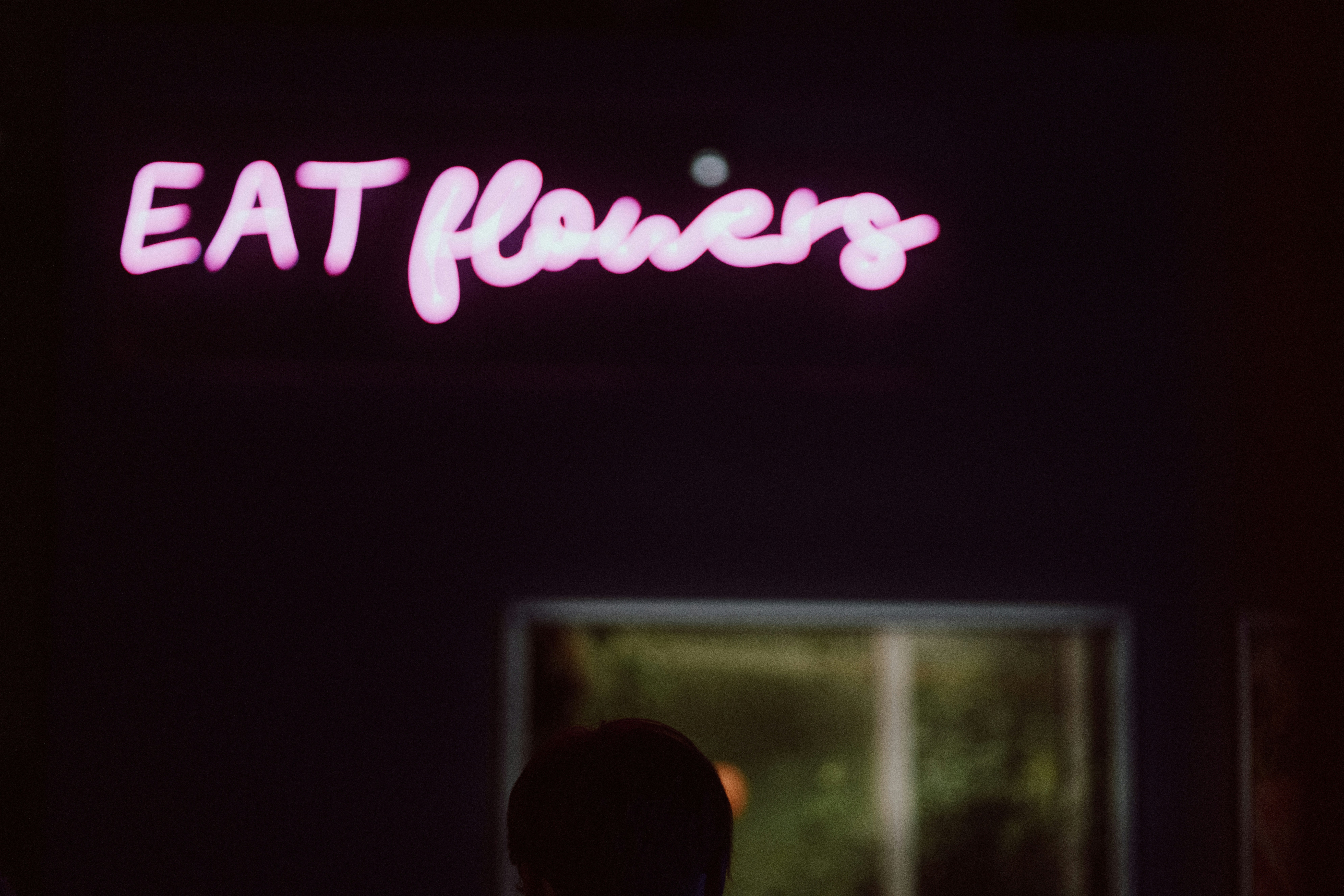 A man standing in front of a neon sign that says eat flowers photo