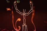 A digital illustration resembling a stylized human figure made of glowing lines against a dark background. The figure appears to be raising its arms, with abstract, flame-like shapes surrounding it.